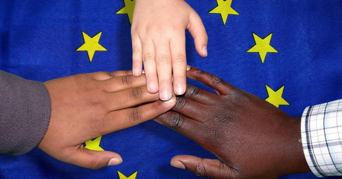 Olika färgs händer på EU:s blåa flagga med gula stjärnor i ring